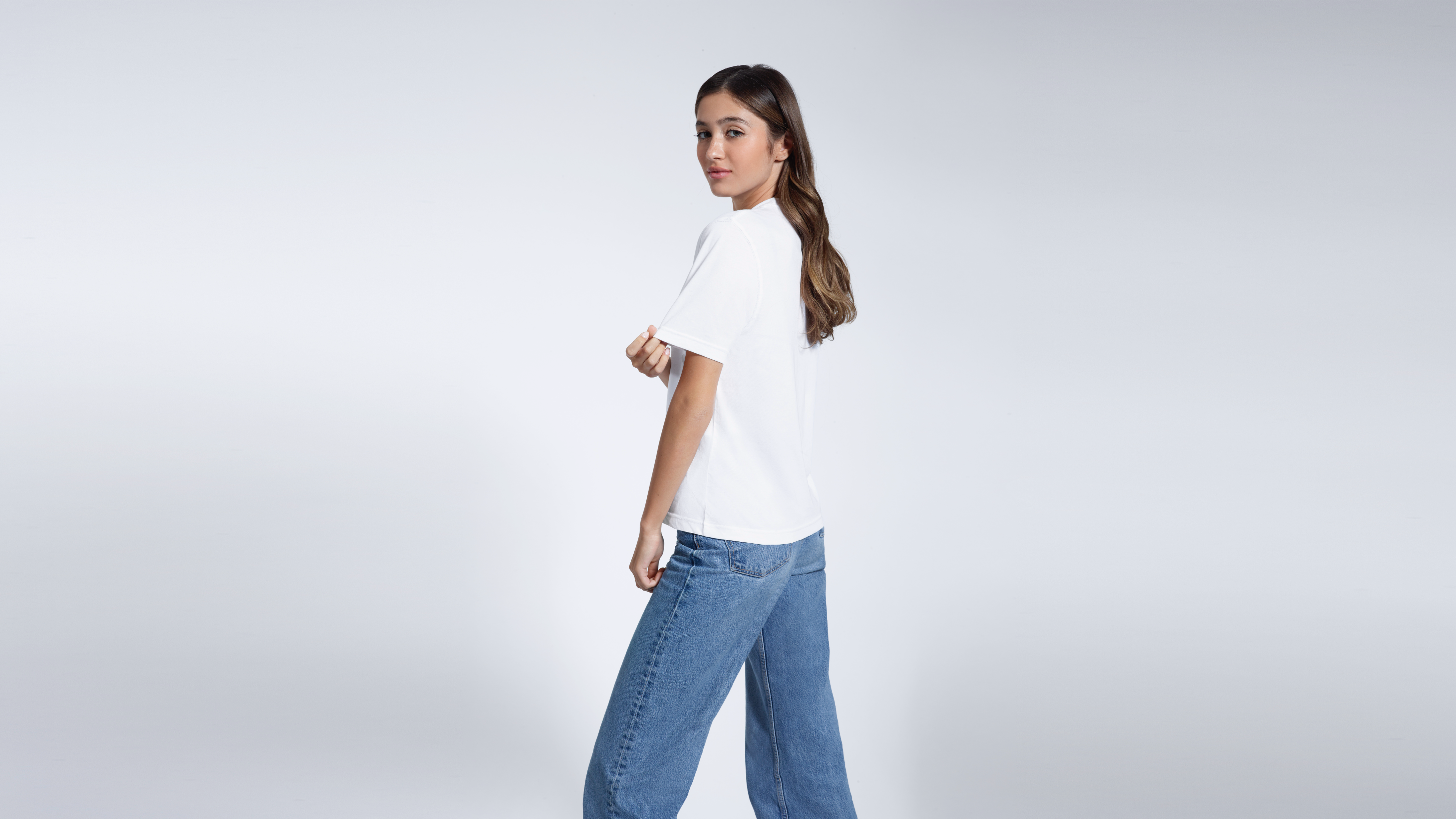 A woman looking back at the camera touching her sleeve, modelling a plain white organic cotton t shirt.