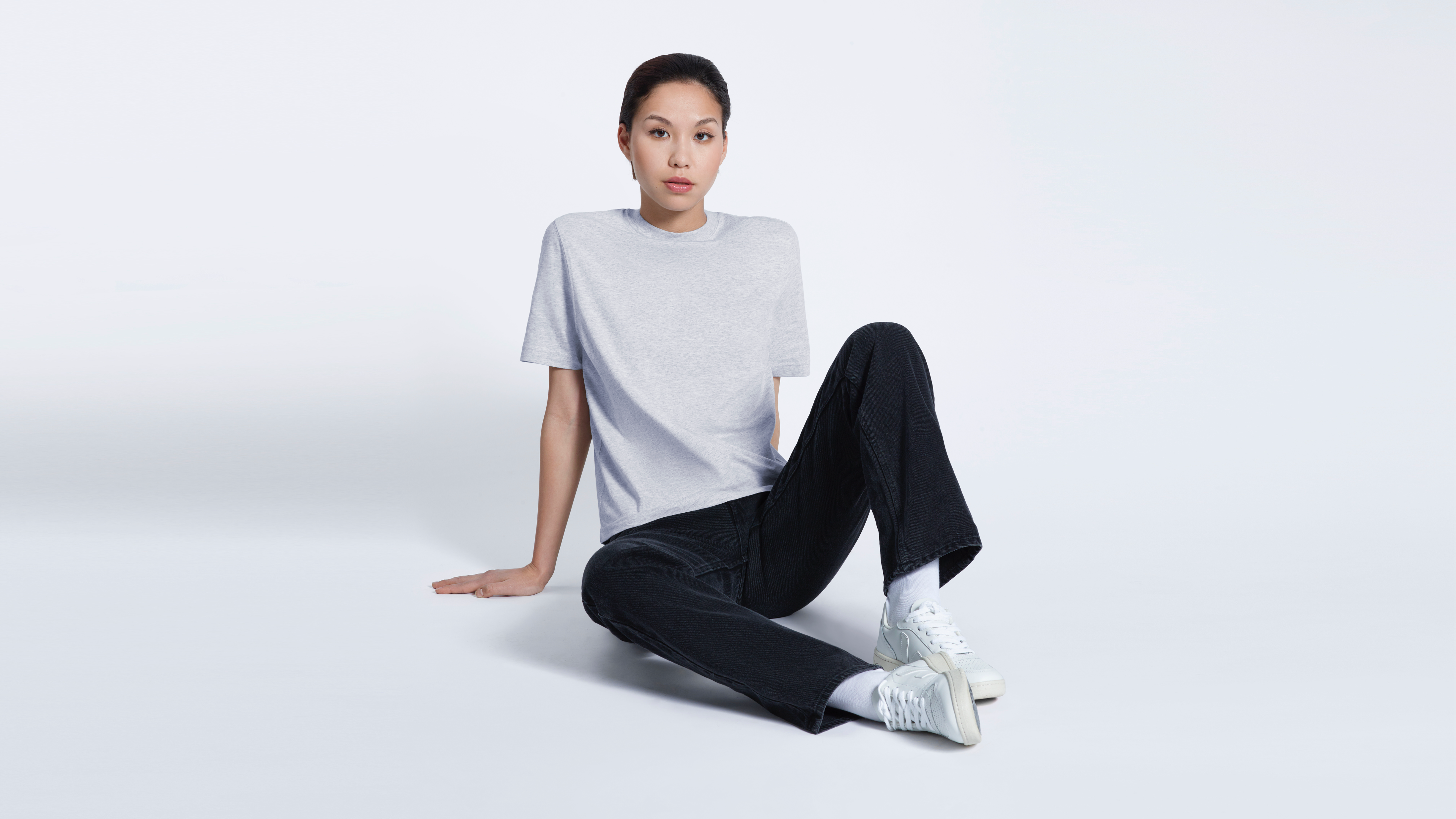 A woman sitting on the floor looking into the camera, modelling a plain grey short sleeve organic cotton t shirt.