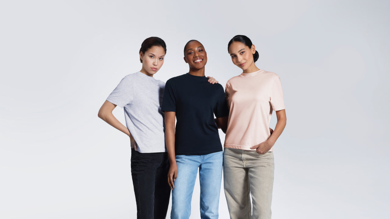 Three women looking into the camera, modelling plain grey, navy and pink organic cotton crew neck t shirts.