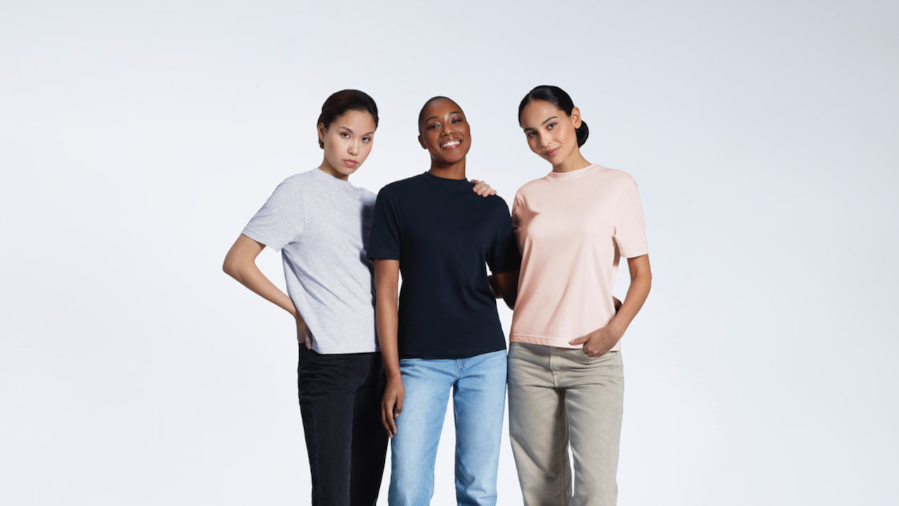 Three women looking into the camera, modelling plain grey, navy and pink organic cotton crew neck t shirts.