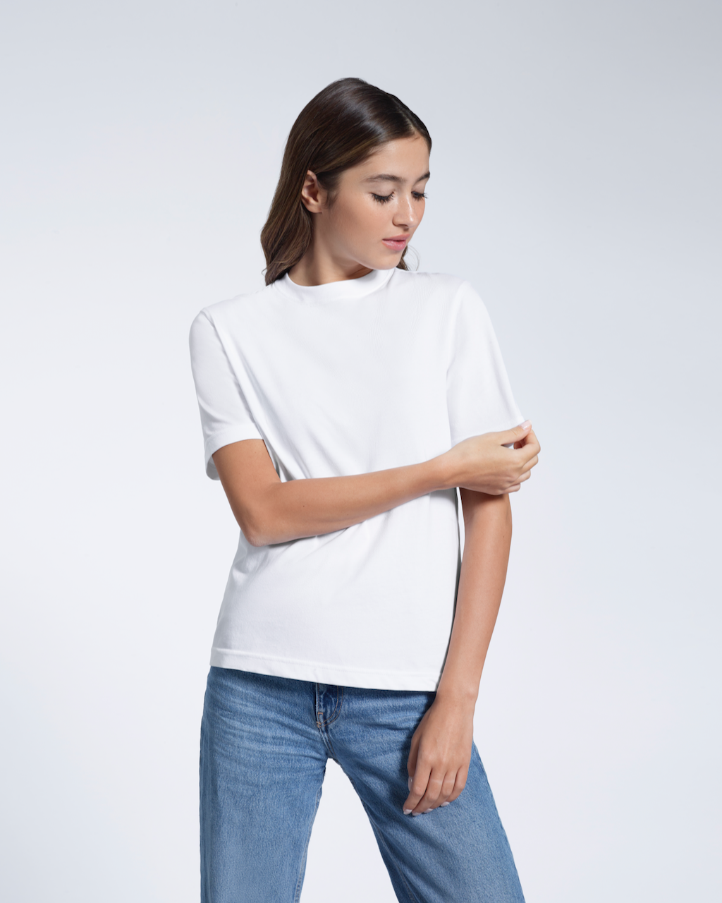 A woman looking down and touching her sleeve, modelling a plain white short sleeve organic cotton t shirt.