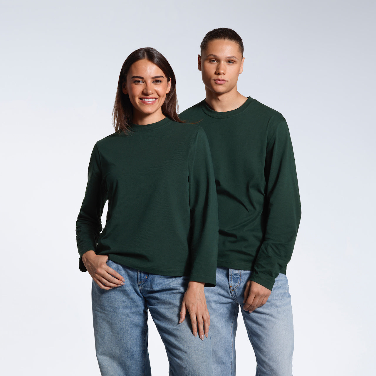 A man and woman looking into the camera, modelling matching plain green long sleeve organic cotton t shirts.