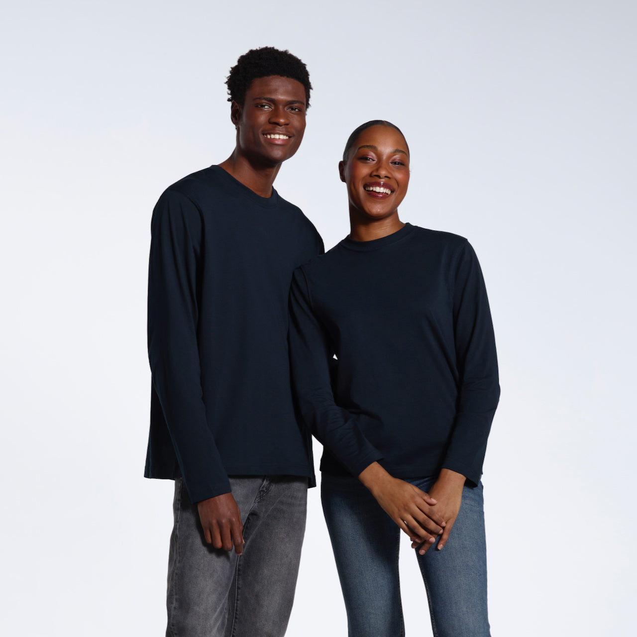 A man and woman smiling into the camera, modelling plain, navy, long sleeve, organic cotton t shirts.