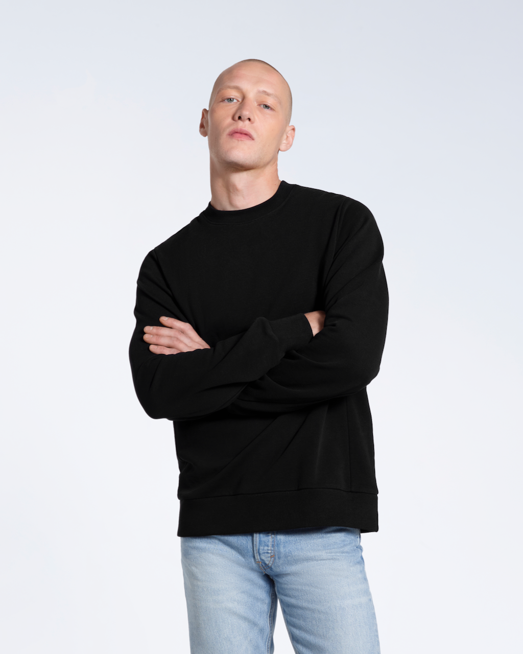 A man looking into the camera with his arms crossed, modelling a plain black french terry organic cotton sweatshirt.