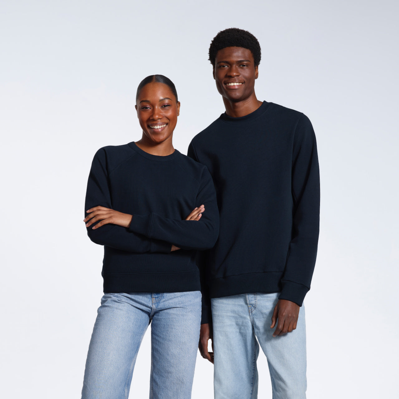 A man and woman smiling, modelling plain navy organic cotton sweatshirts.