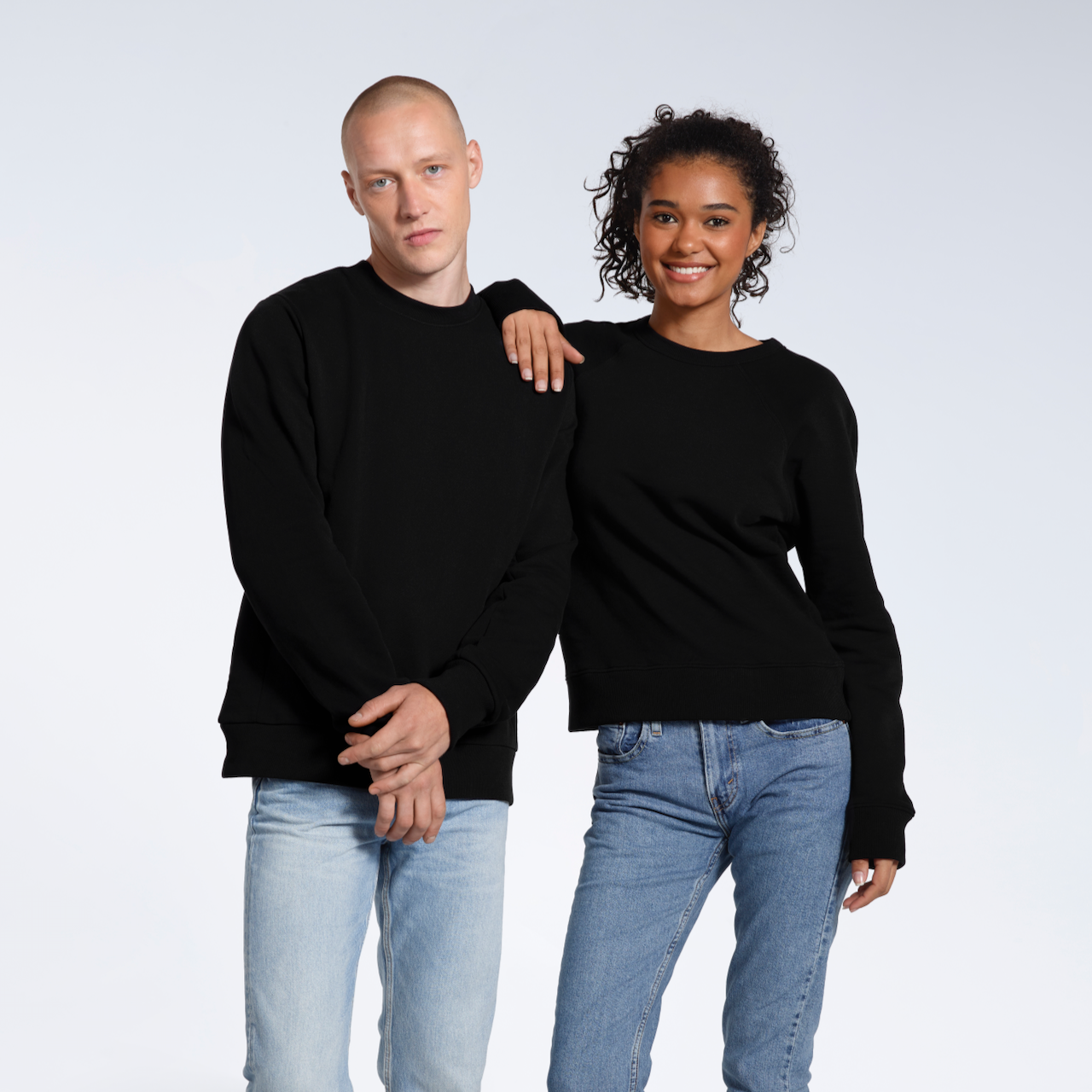 A man and woman looking into the camera, modelling matching plain black, organic cotton sweatshirts.