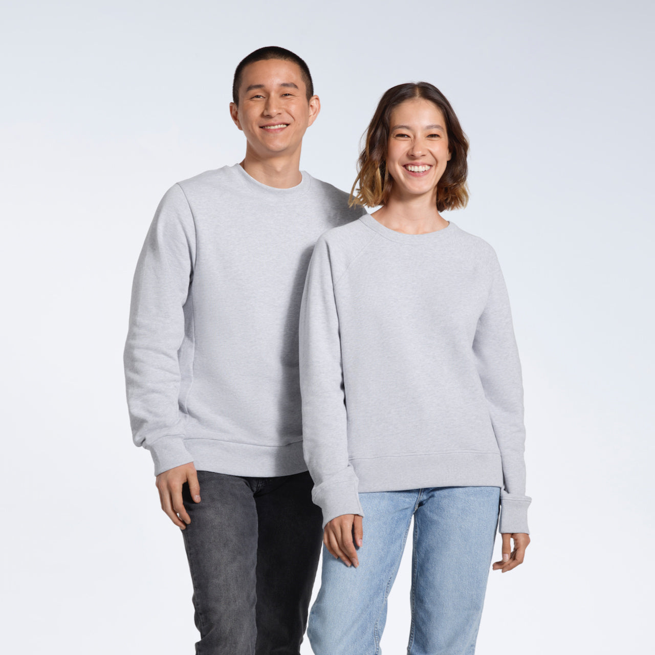 A man and woman smiling into the camera, modelling grey organic cotton sweatshirts.