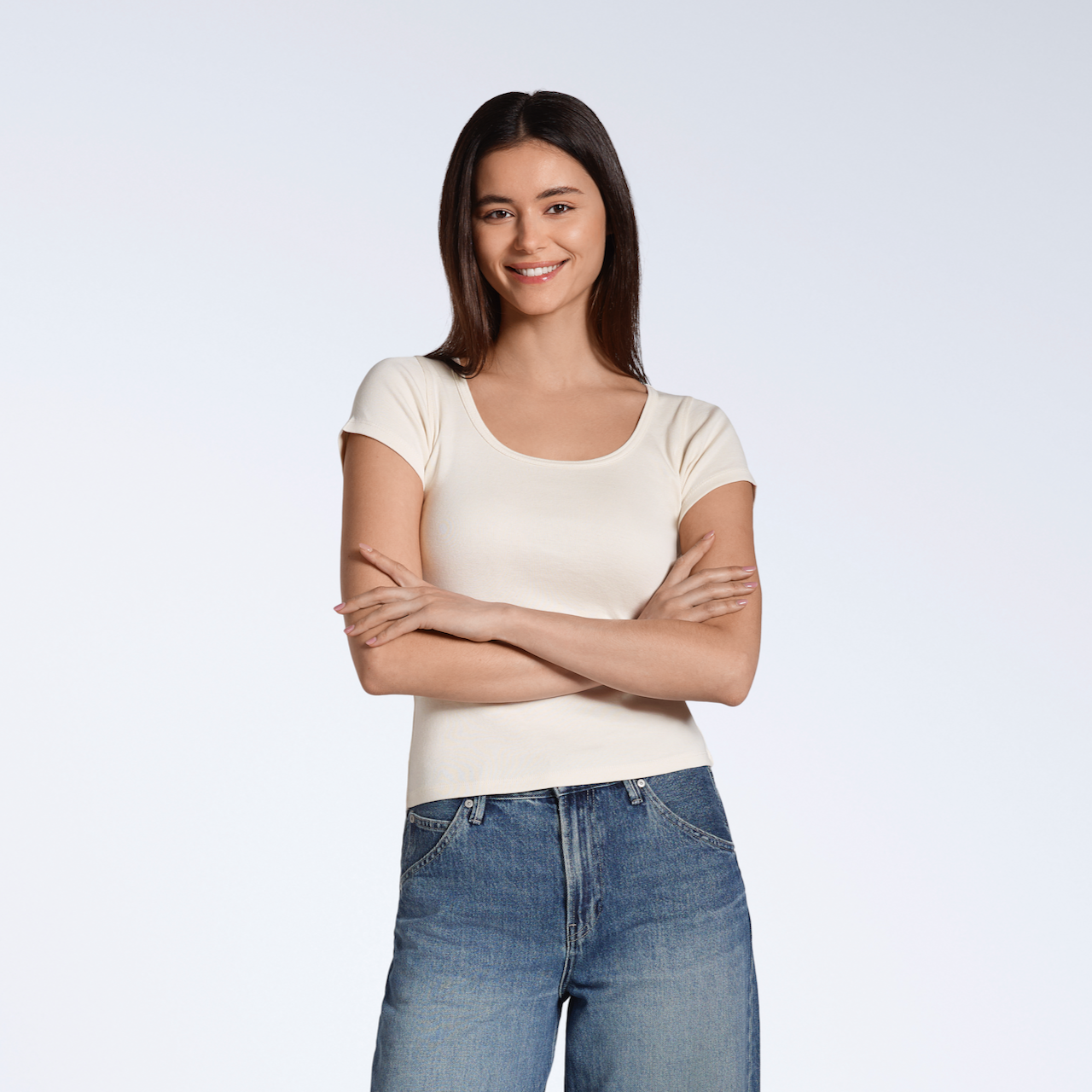 A woman with her arms crossed smiling into the camera, modelling a plain natural, organic cotton scoop neck t shirt.