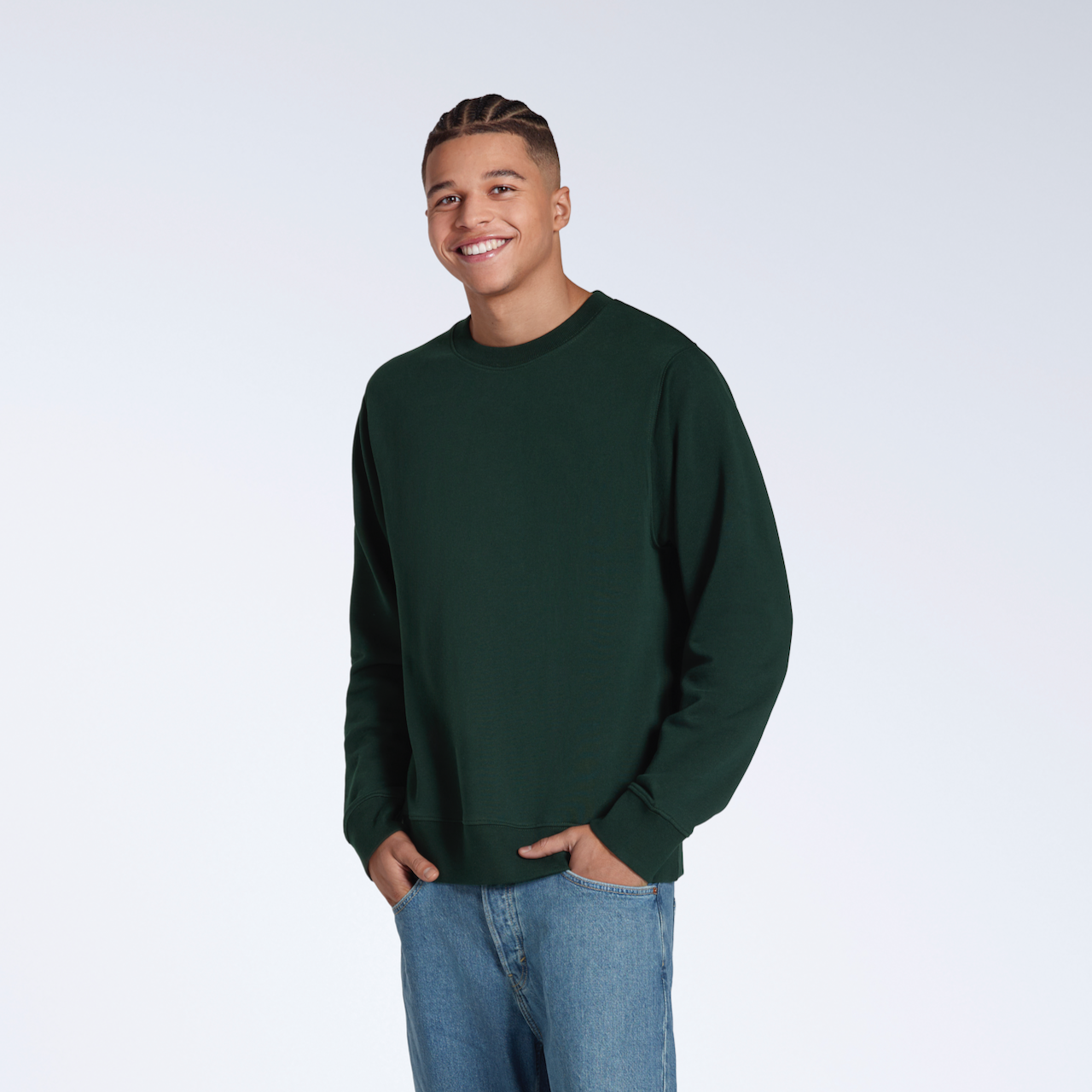 A man smiling into the camera with his hands in his pockets, modelling a plain dark green french terry organic cotton sweatshirt.