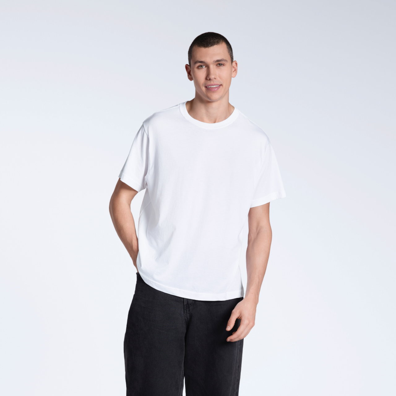 A man smiling into the camera with a hand in his pocket, modelling a plain white, organic cotton t shirt with a pair of black jeans.