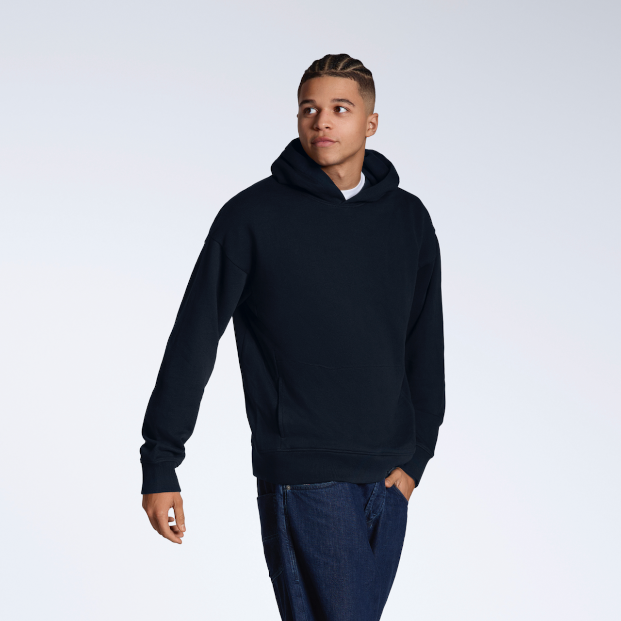 A man looking away from the camera with a hand in his pocket, modelling a navy oversized organic cotton hoodie.