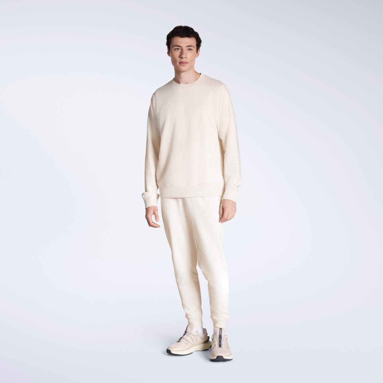 A full body photo of a man modelling a plain, matching, natural coloured, organic cotton tracksuit.