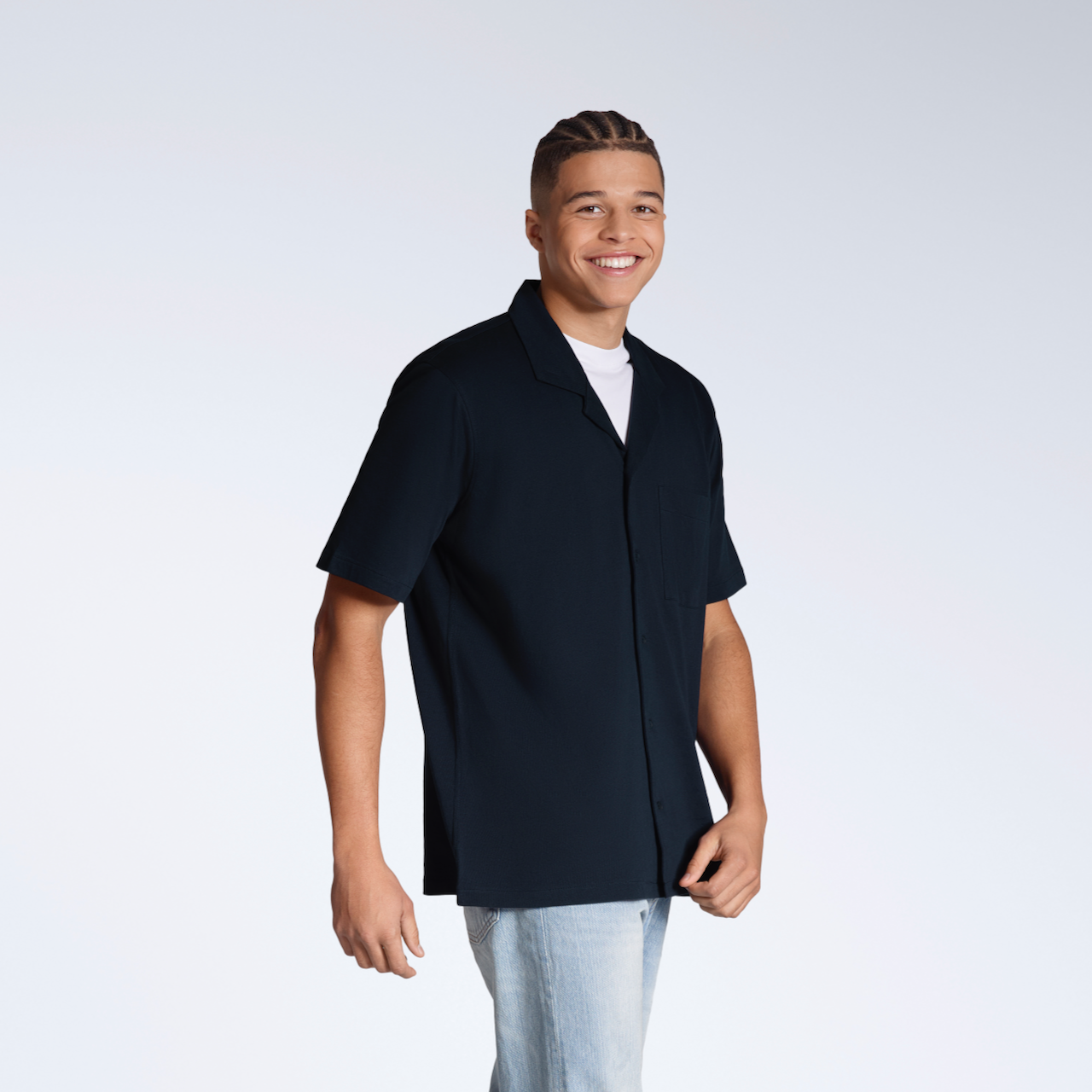A man smiling into the camera, modelling a plain navy, organic cotton, short sleeve resort shirt.