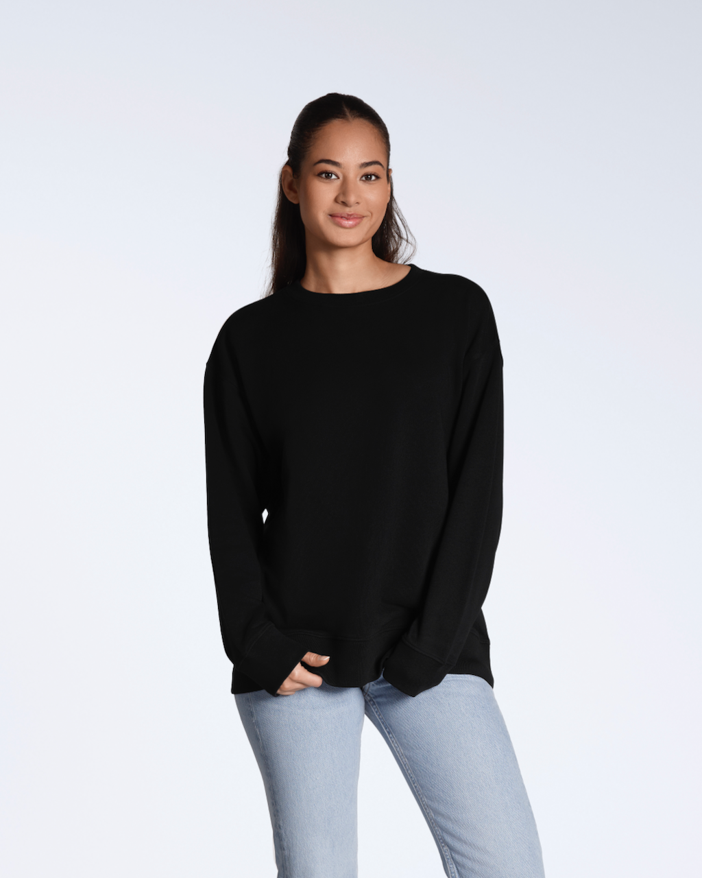 A full body photo of a woman smiling into the camera, modelling a plain black, oversized, organic cotton sweatshirt.