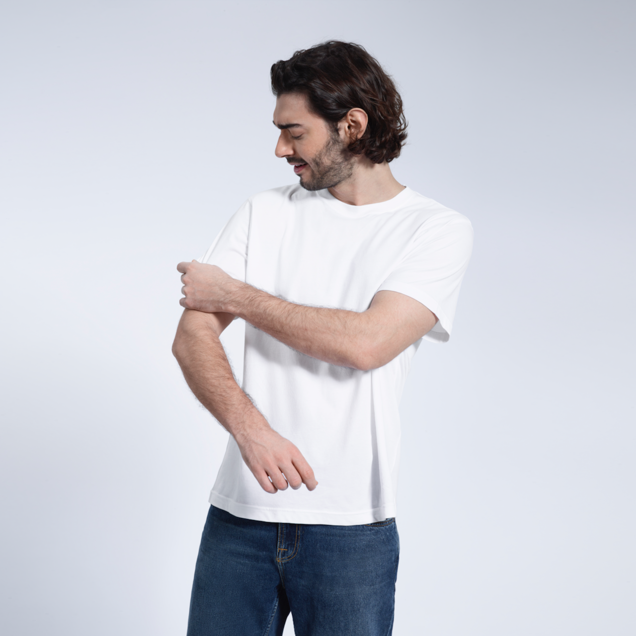A man looking down and touching his sleeve, modelling a plain white short sleeve organic cotton t shirt.