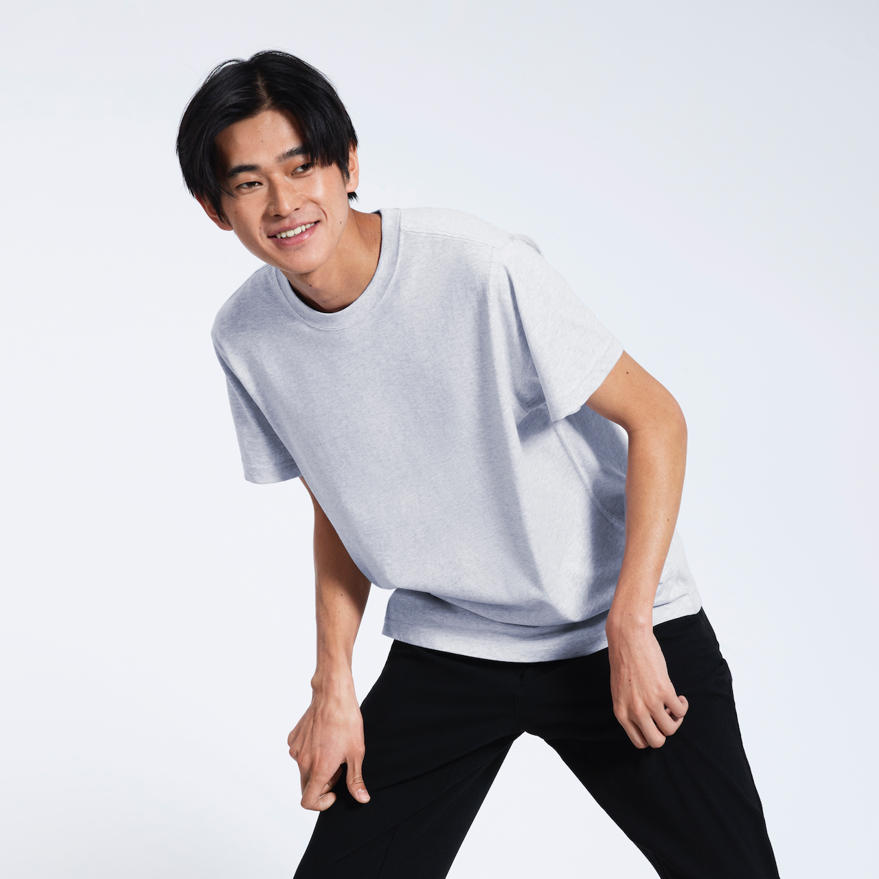 A man leaning over slightly, smiling, modelling a plain short sleeve grey organic cotton t shirt.