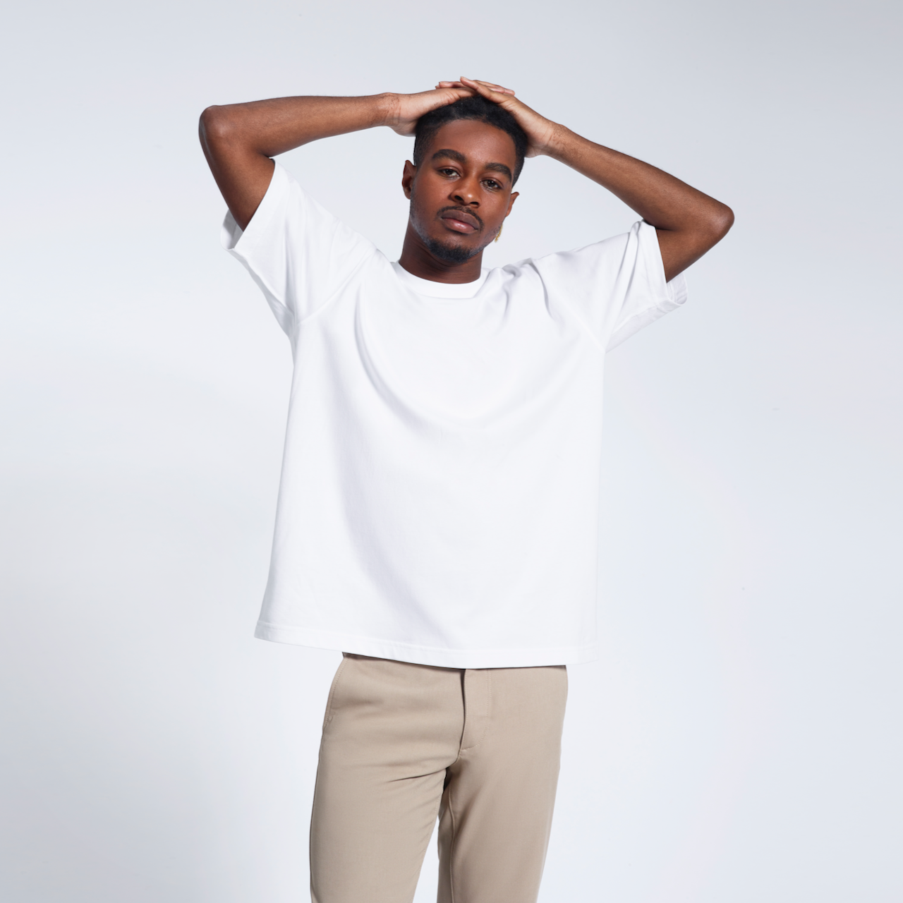 A man looking into the camera with his hands on his head, modelling plain a white oversized heavyweight organic cotton t shirt.