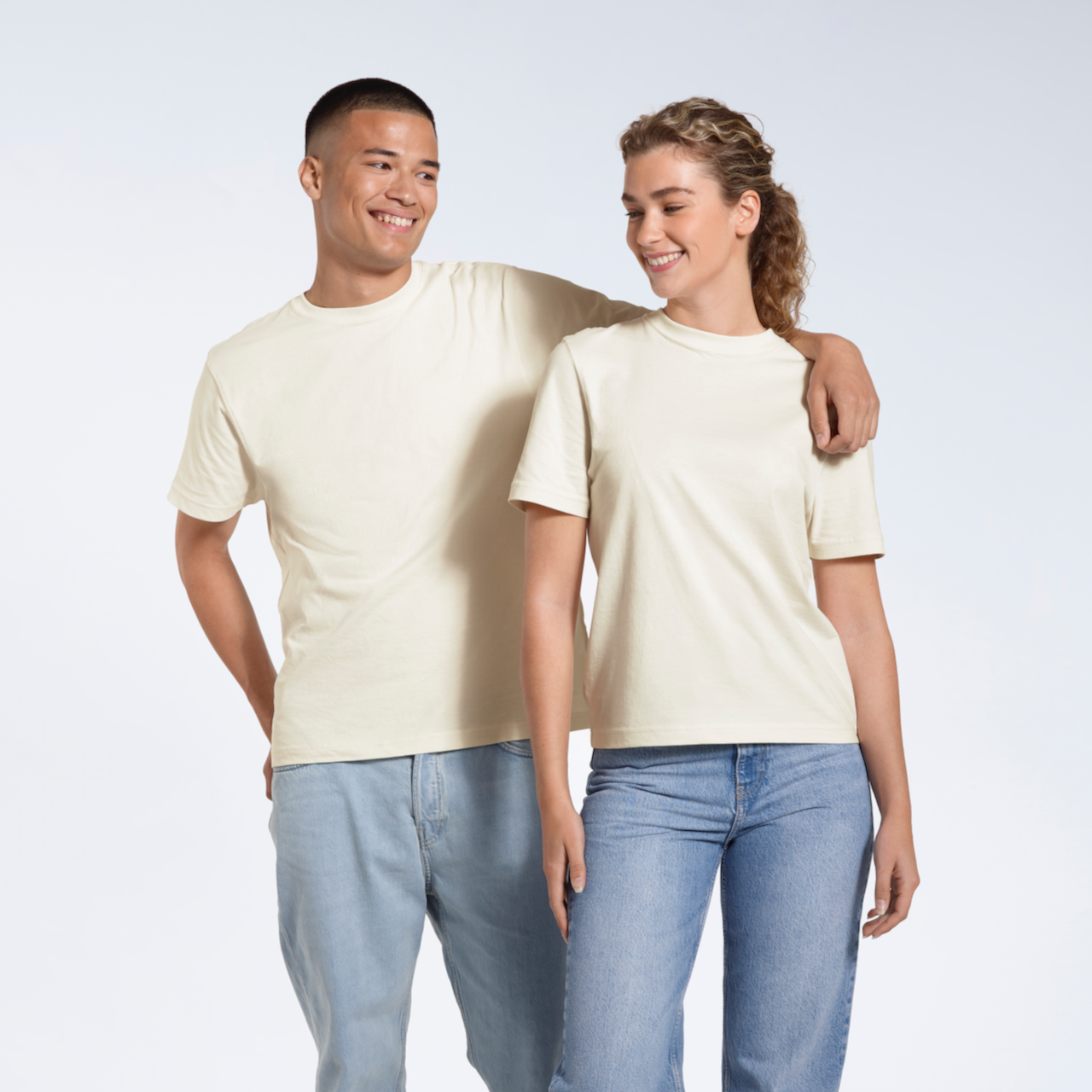 A man and woman smiing at eachother, modelling matching plain, ecru, organic cotton t shirts.