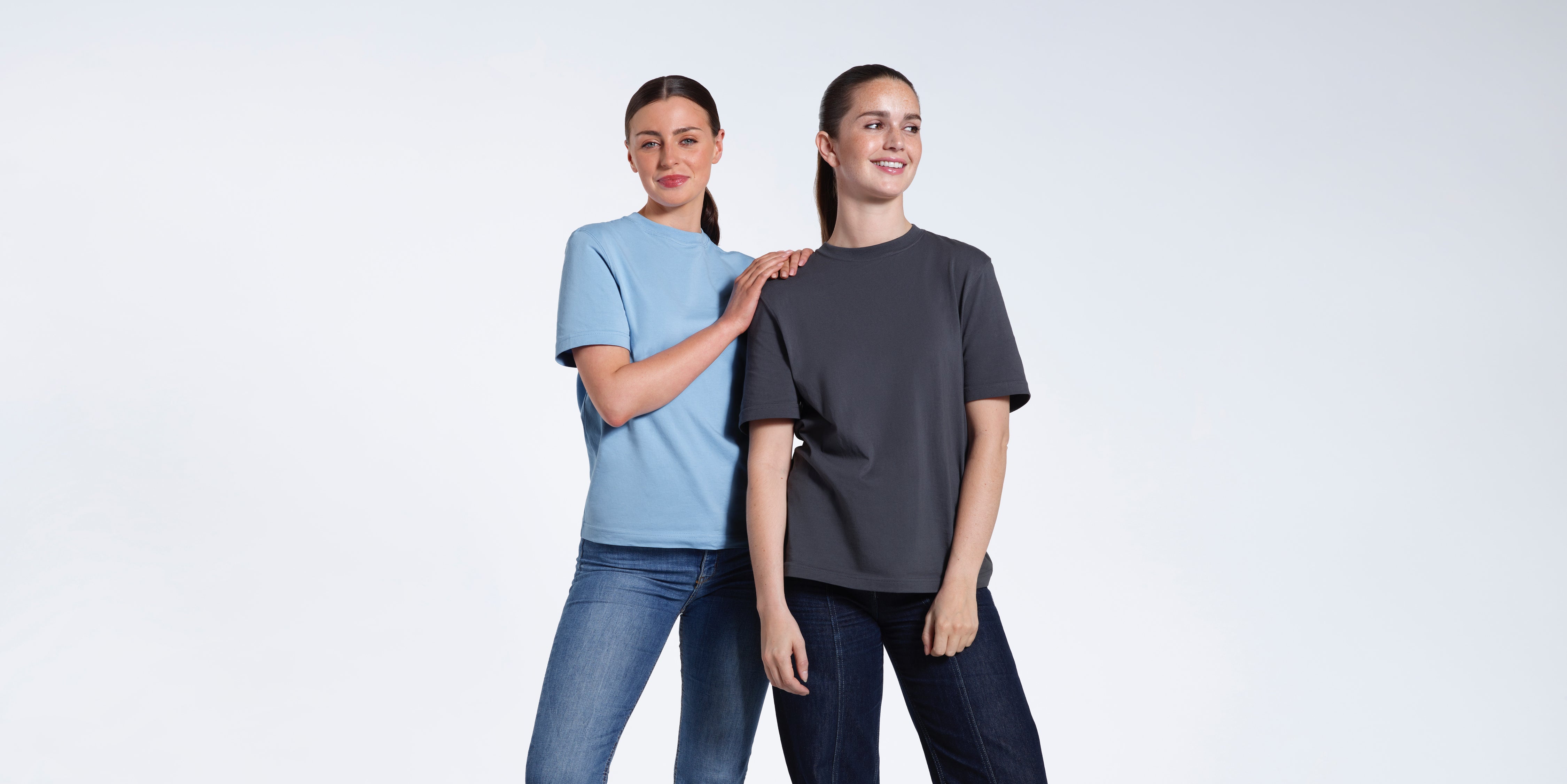 Two women smiling, modelling light blue and dark grey organic cotton crew neck t shirts.