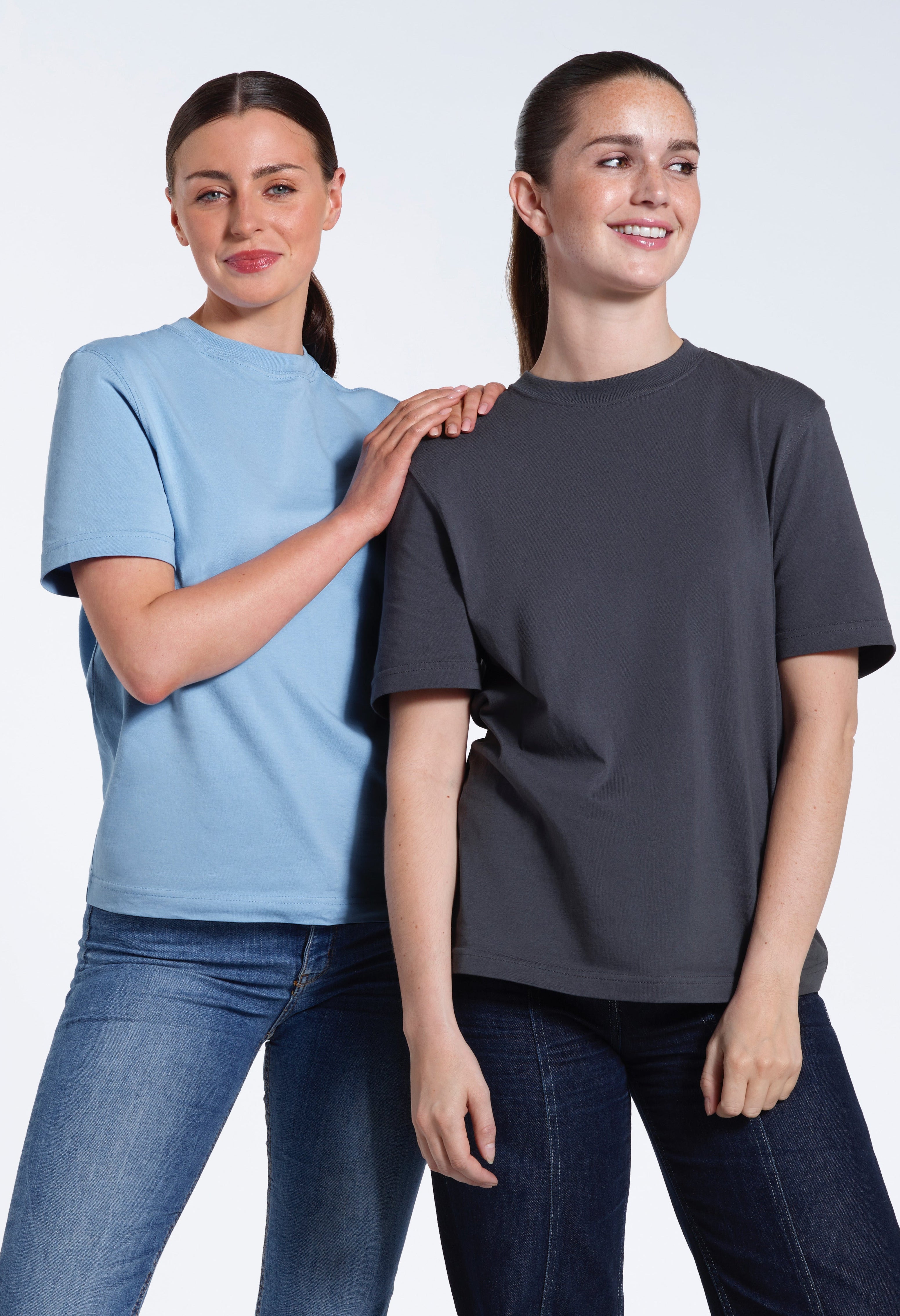 Two women smiling, modelling light blue and dark grey organic cotton crew neck t shirts.