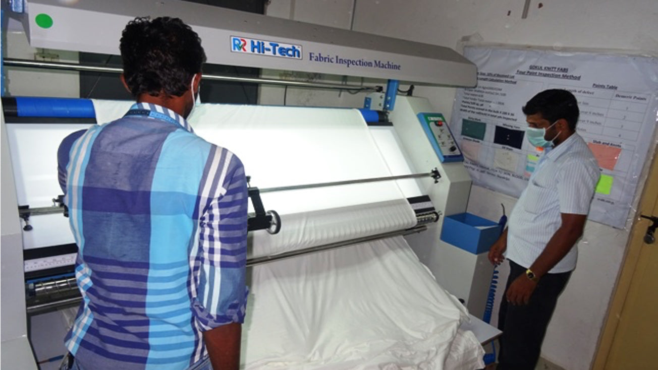 A photo of 2 factory workers checking the fabric using a large machine in an ethical factory in India.