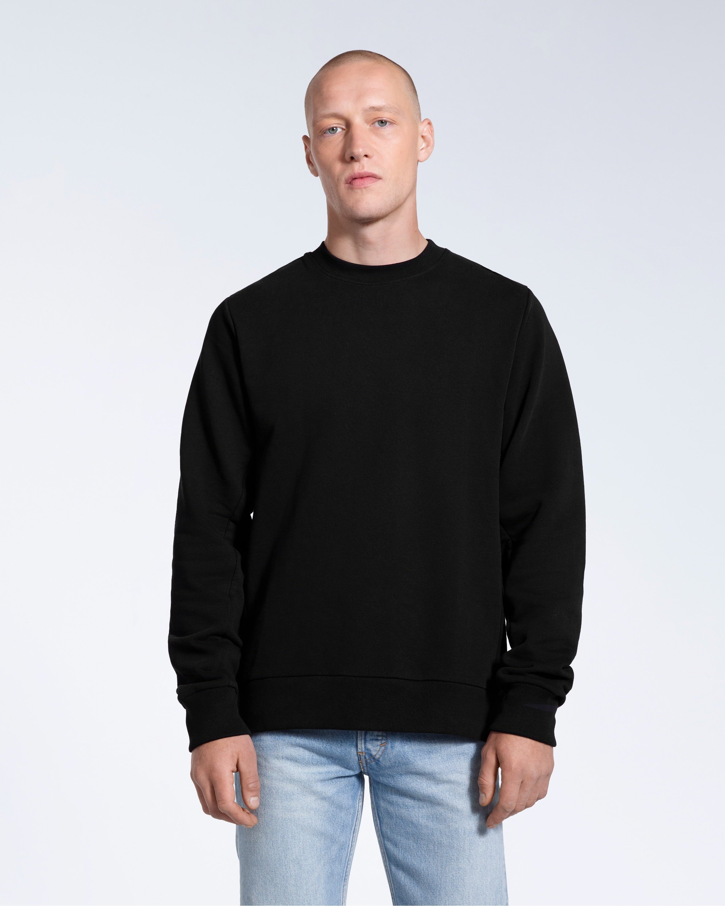 A man face on looking into the camera with his arms by his side, modelling a plain black french terry organic cotton sweatshirt.