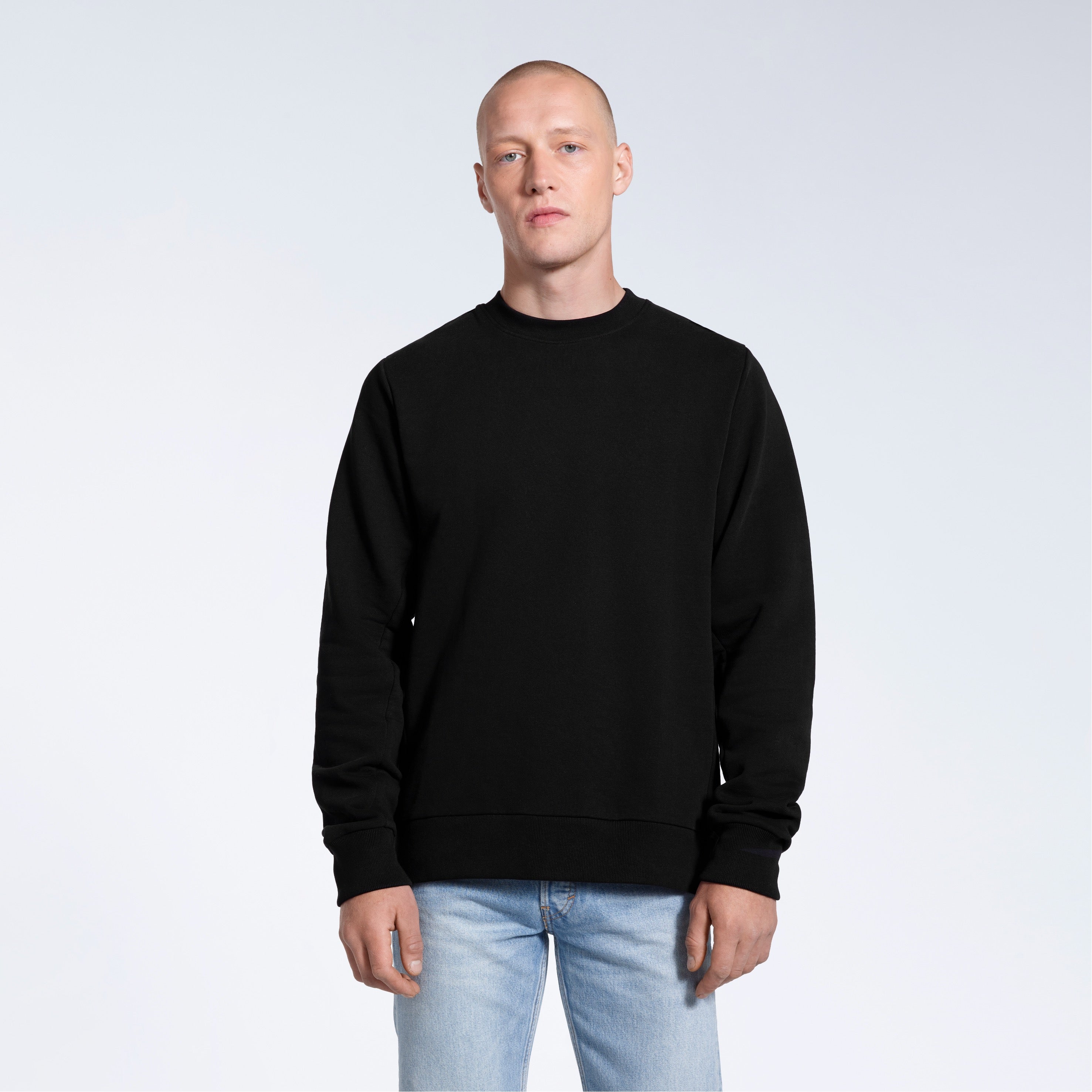 A man face on looking into the camera with his arms by his side, modelling a plain black french terry organic cotton sweatshirt.