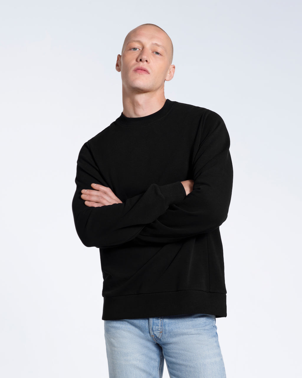 A man looking into the camera with his arms crossed, modelling a plain black french terry organic cotton sweatshirt.