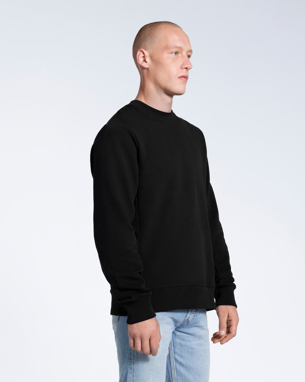 A man looking away from the camera with his arms by his side, modelling a plain black french terry organic cotton sweatshirt.
