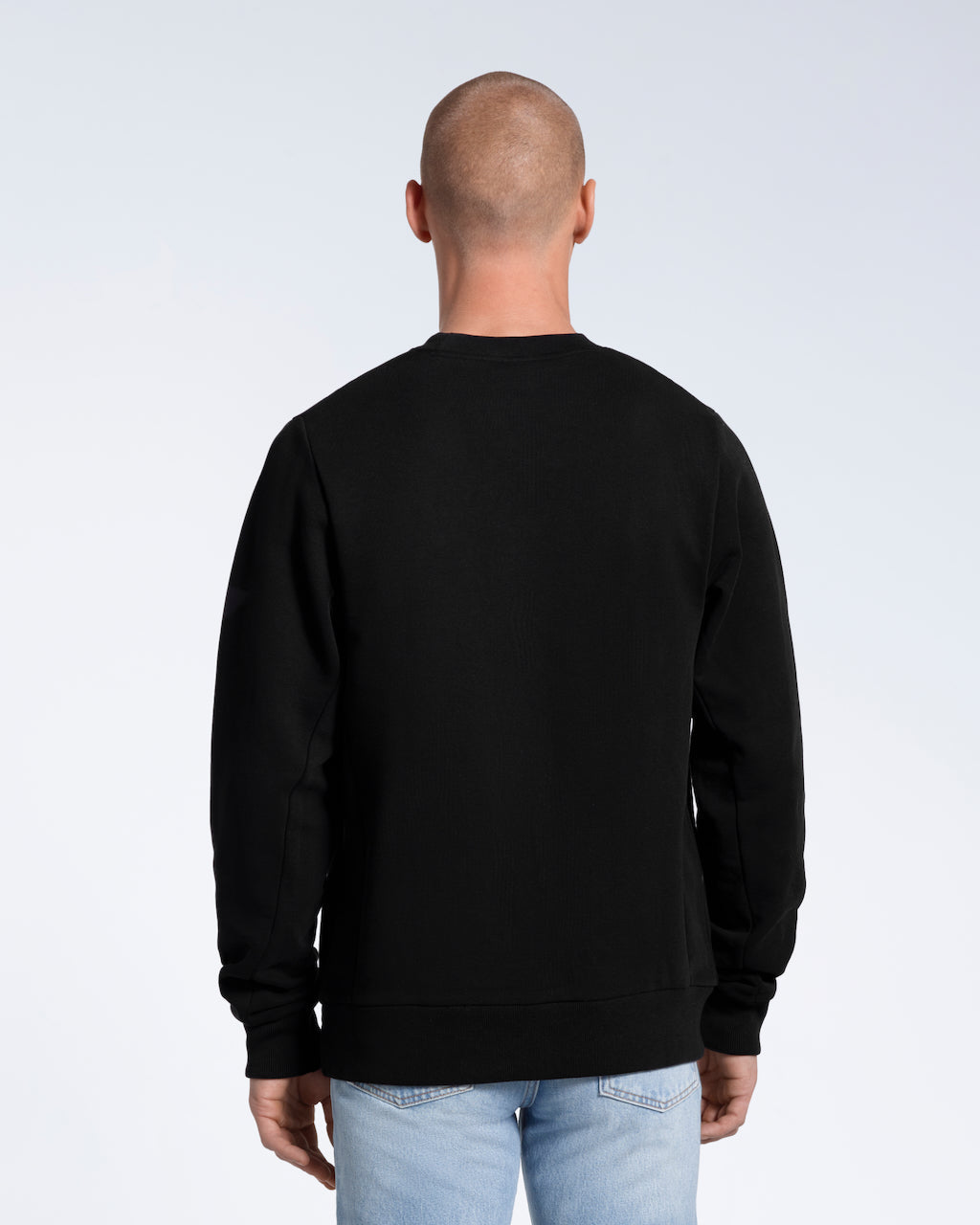 A man facing away from the camera, showing the back of his plain black french terry organic cotton sweatshirt.