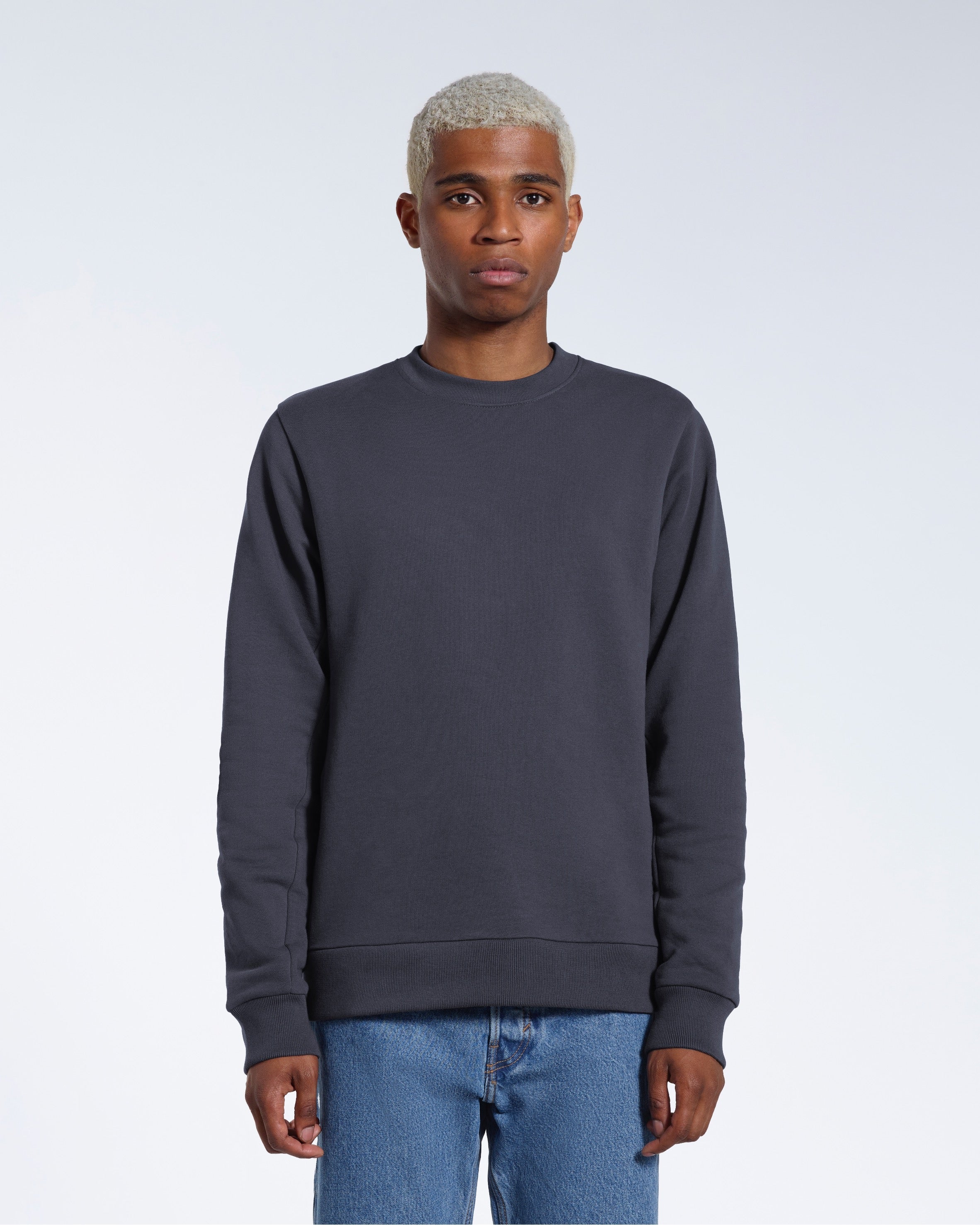 A man face on looking into the camera with his arms by his side, modelling a plain dark grey french terry organic cotton sweatshirt.