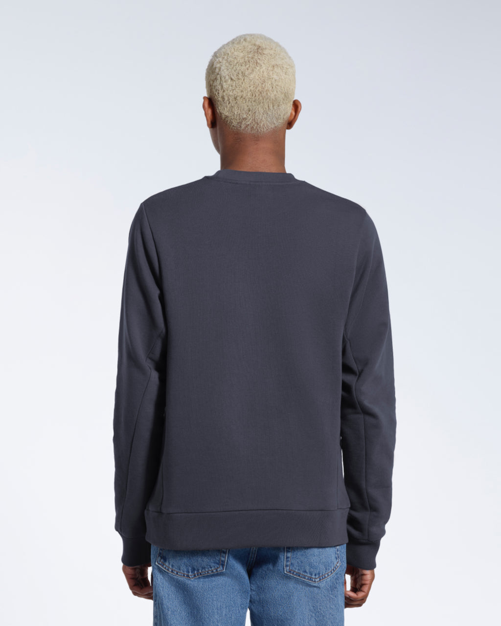 A man facing away from the camera, showing the back of his plain dark grey french terry organic cotton sweatshirt.