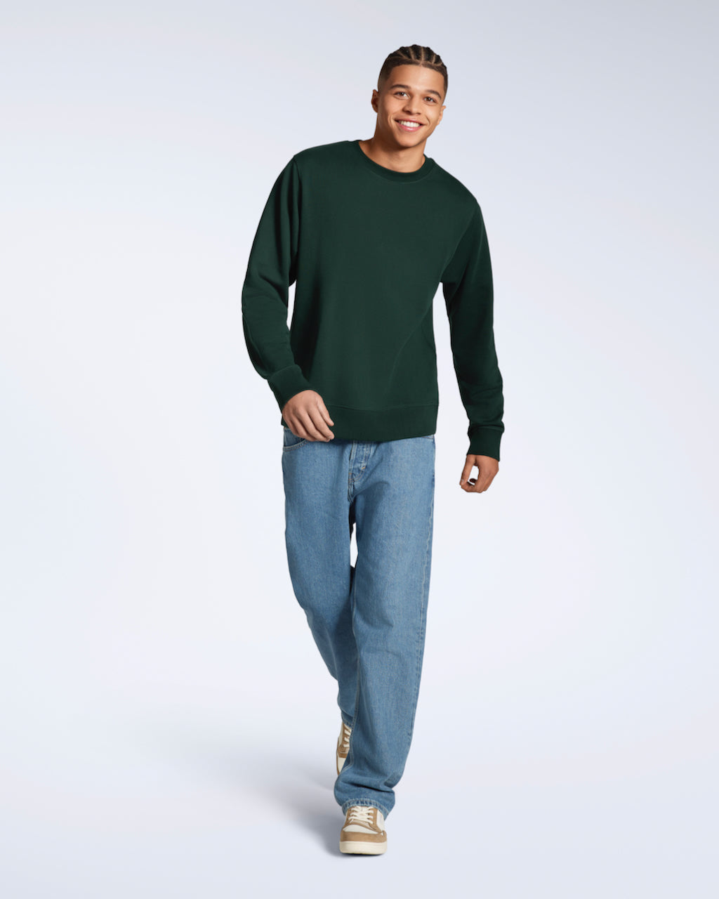 A full body photo of a man walking smiling into the camera, modelling a plain dark green french terry organic cotton sweatshirt.
