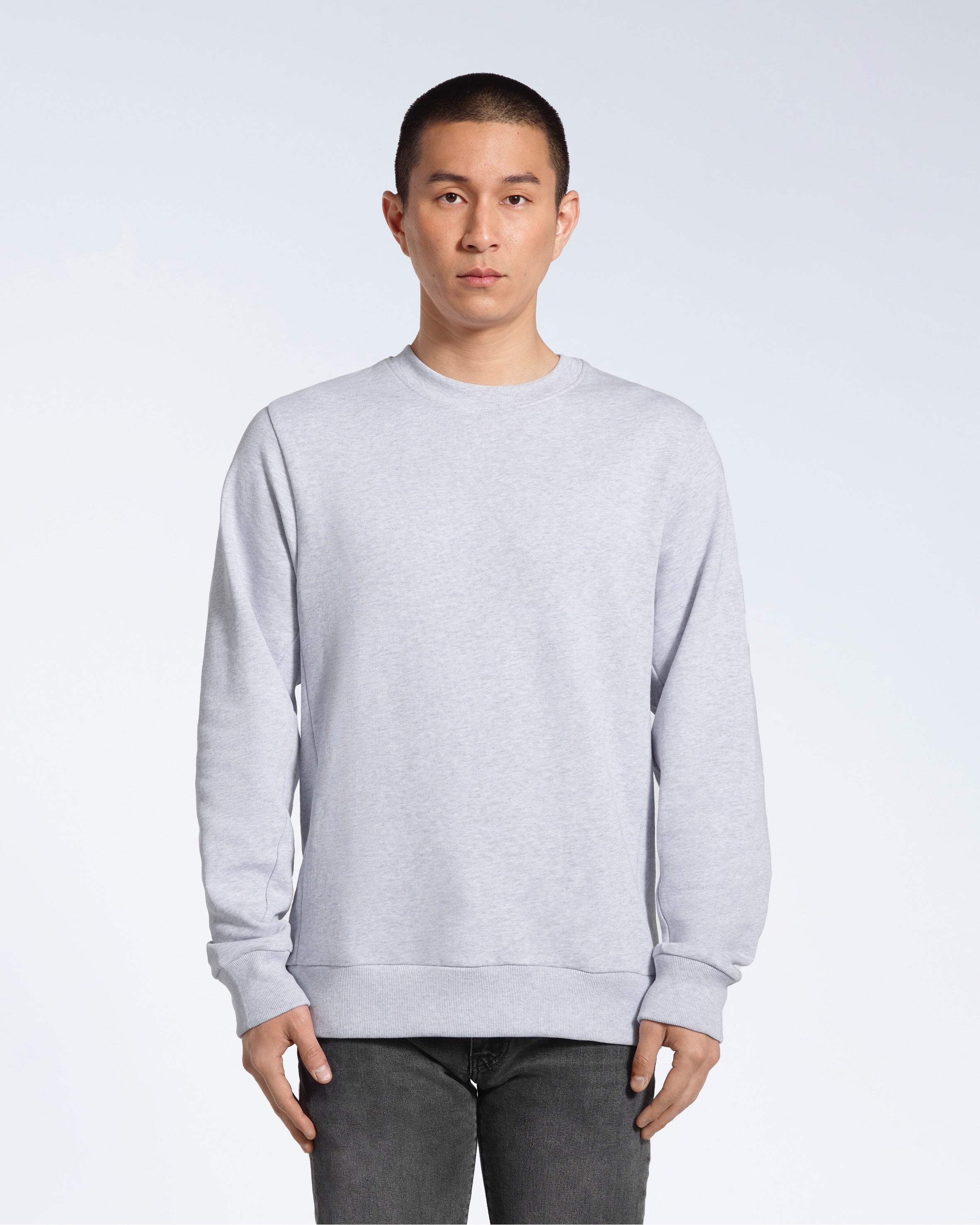 A man face on looking into the camera with his arms by his side, modelling a plain grey french terry organic cotton sweatshirt.