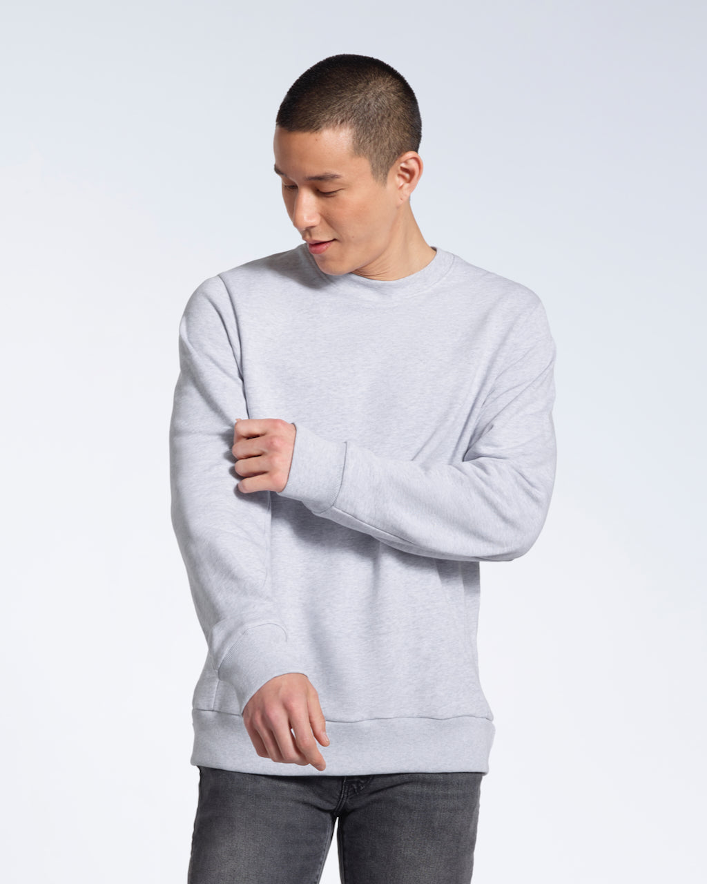 A man looking down, touching the sleeve of his plain grey french terry organic cotton sweatshirt.