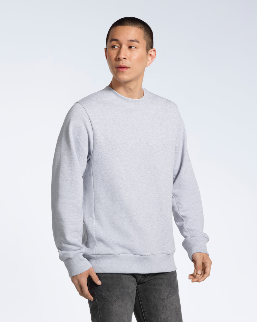 A man looking away from the camera with his arms by his side, modelling a plain grey french terry organic cotton sweatshirt.