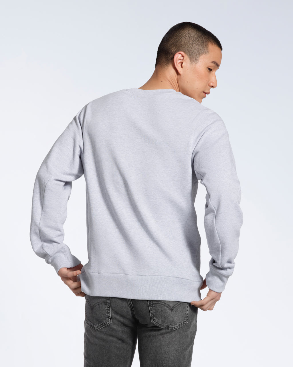 A man facing away from the camera, showing the back of his plain grey french terry organic cotton sweatshirt.