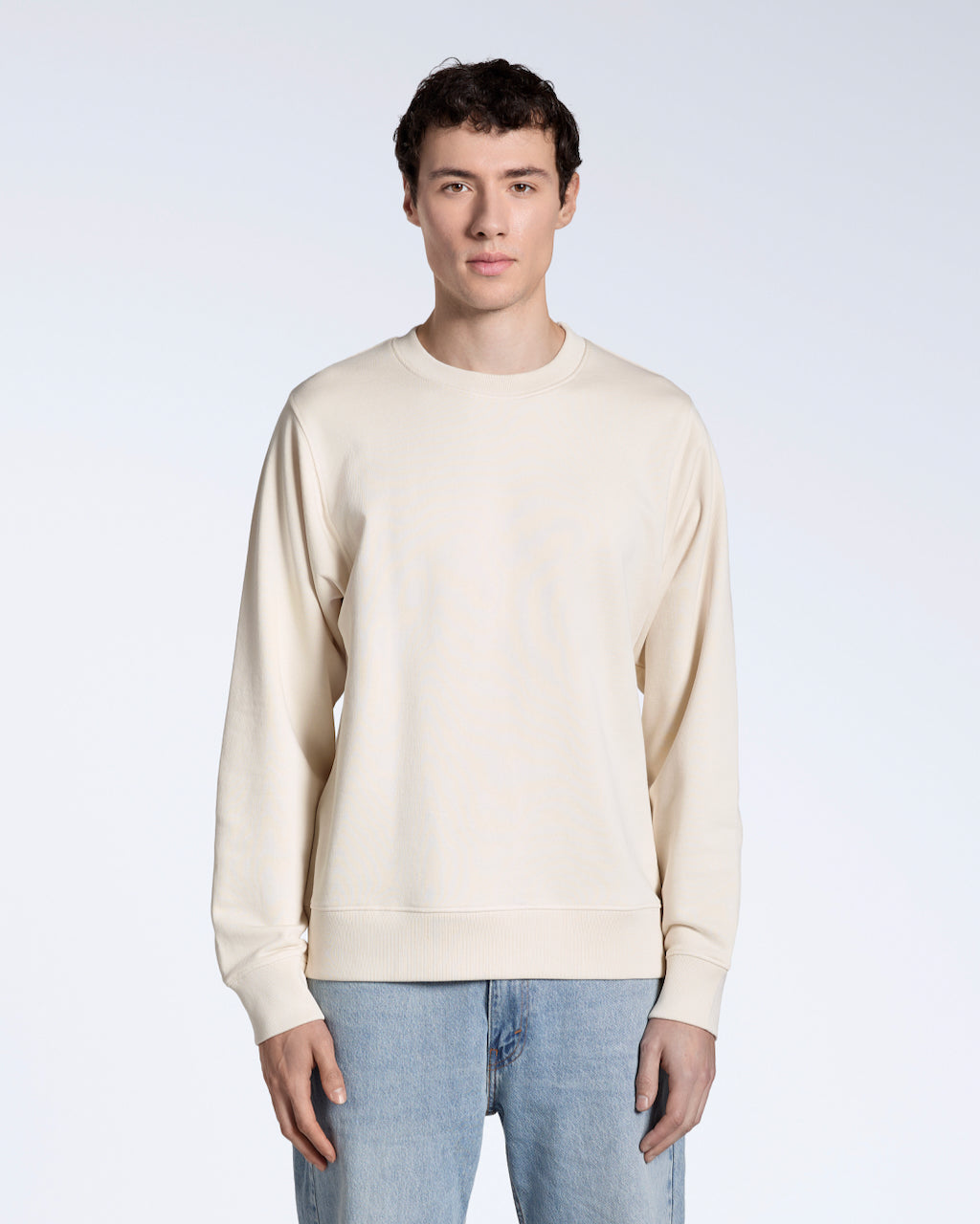 A man facing front on, looking into the camera with his arms by his side, modelling a plain natural coloured, organic cotton sweatshirt.