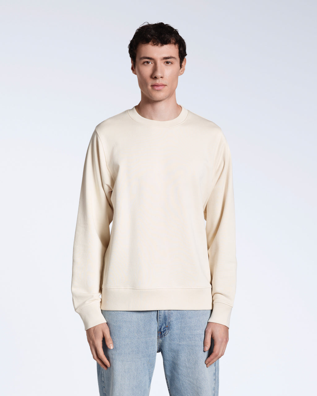A man facing front on, looking into the camera with his arms by his side, modelling a plain natural coloured, organic cotton sweatshirt.