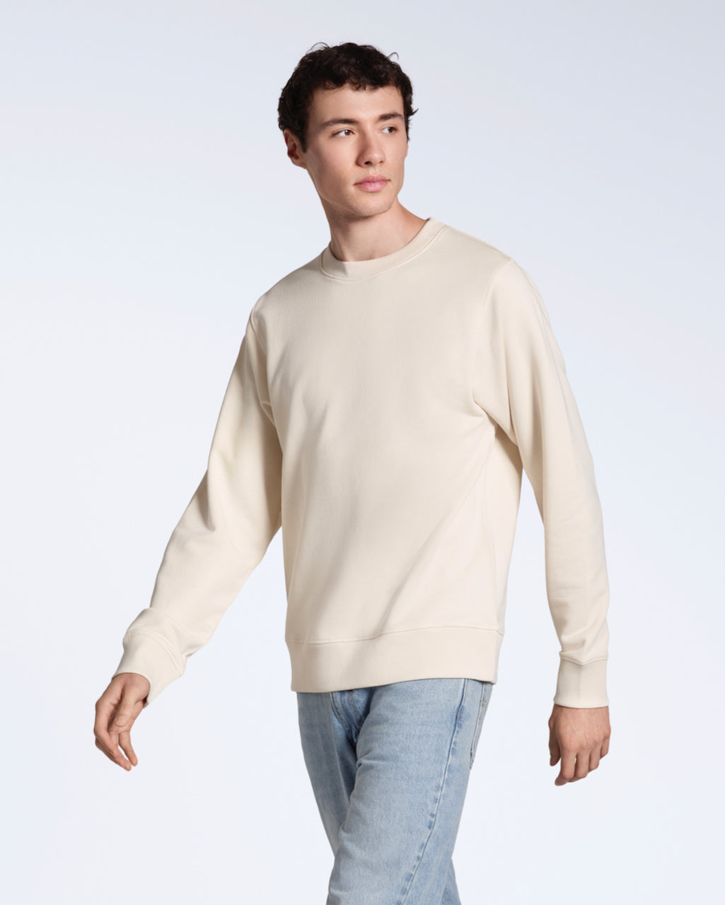 A man looking away from the camera, modelling a plain natural coloured, organic cotton sweatshirt with a pair of blue jeans.