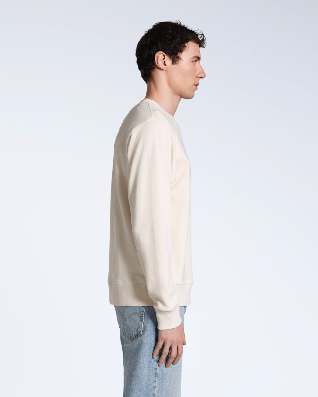 A man facing side on, with his arms by his side, modelling a plain natural coloured, organic cotton sweatshirt.