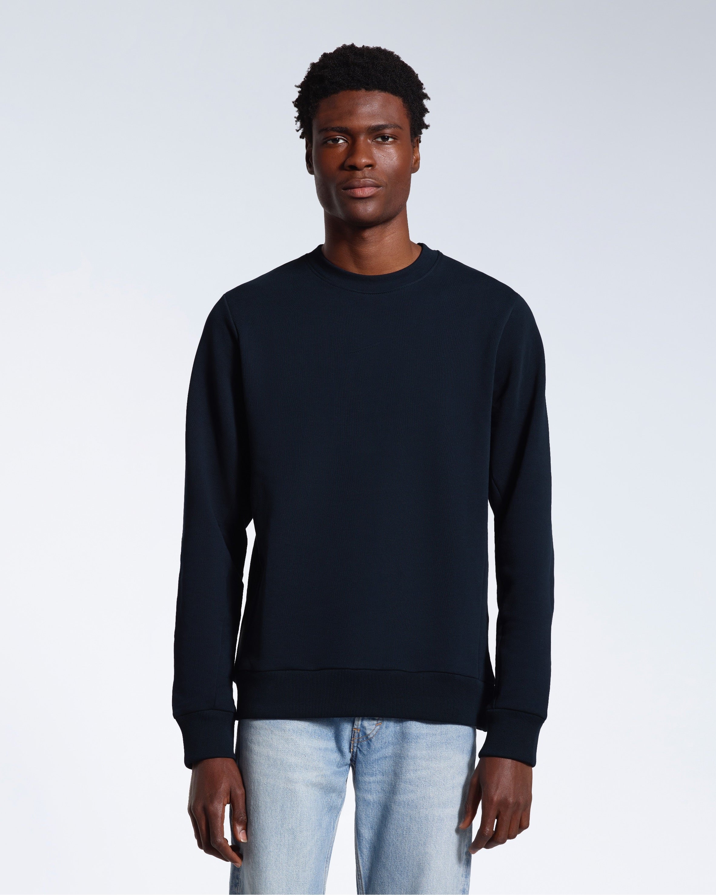 A man face on looking into the camera with his arms by his side, modelling a plain navy french terry organic cotton sweatshirt.