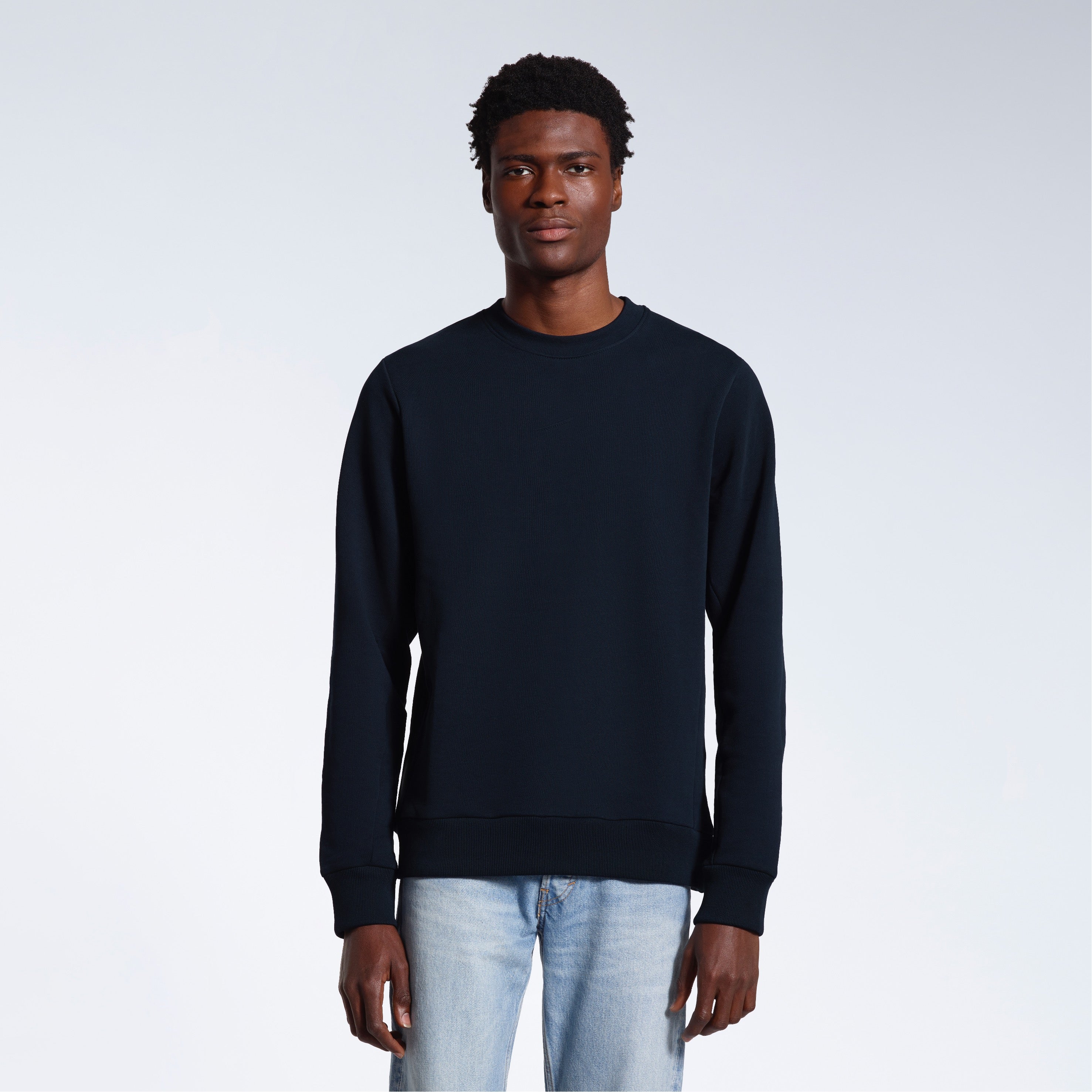 A man face on looking into the camera with his arms by his side, modelling a plain navy french terry organic cotton sweatshirt.