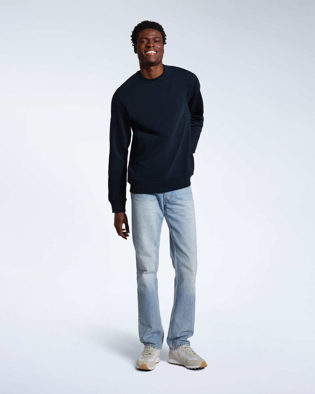 A full body photo of a man smiling into the camera, modelling a plain navy french terry organic cotton sweatshirt.