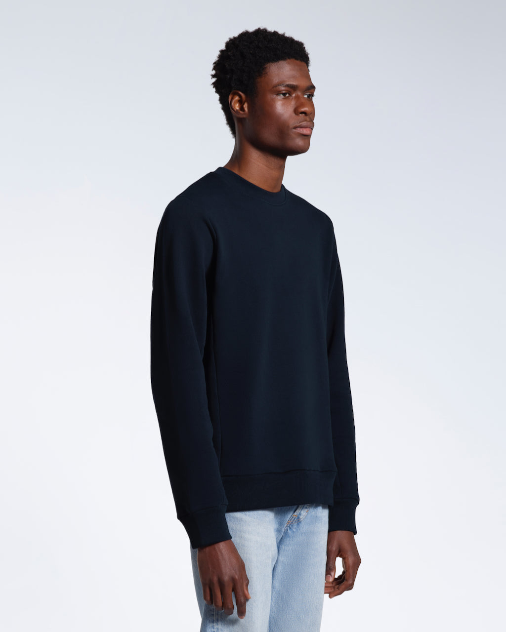 A man looking away from the camera with his arms by his side, modelling a plain navy french terry organic cotton sweatshirt.