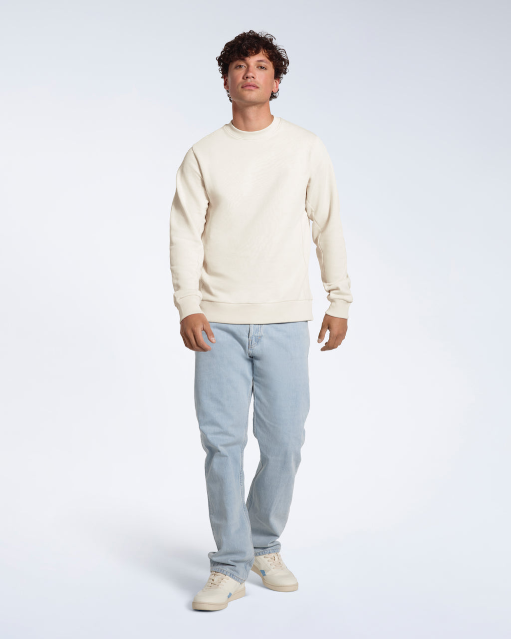 A full body photo of a man looking into the camera, modelling a plain off white french terry organic cotton sweatshirt.