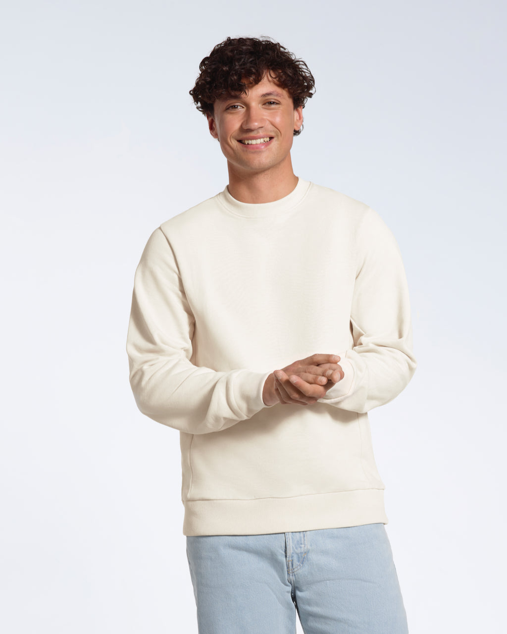 A man smiling into the camera with his hands together, modelling a plain off white french terry organic cotton sweatshirt.