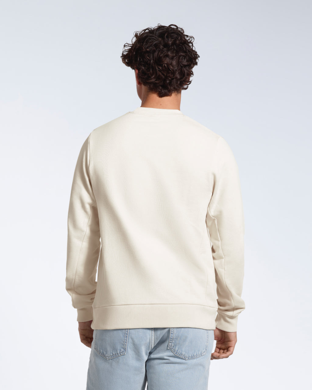 A man facing away from the camera, showing the back of his plain off white french terry organic cotton sweatshirt.