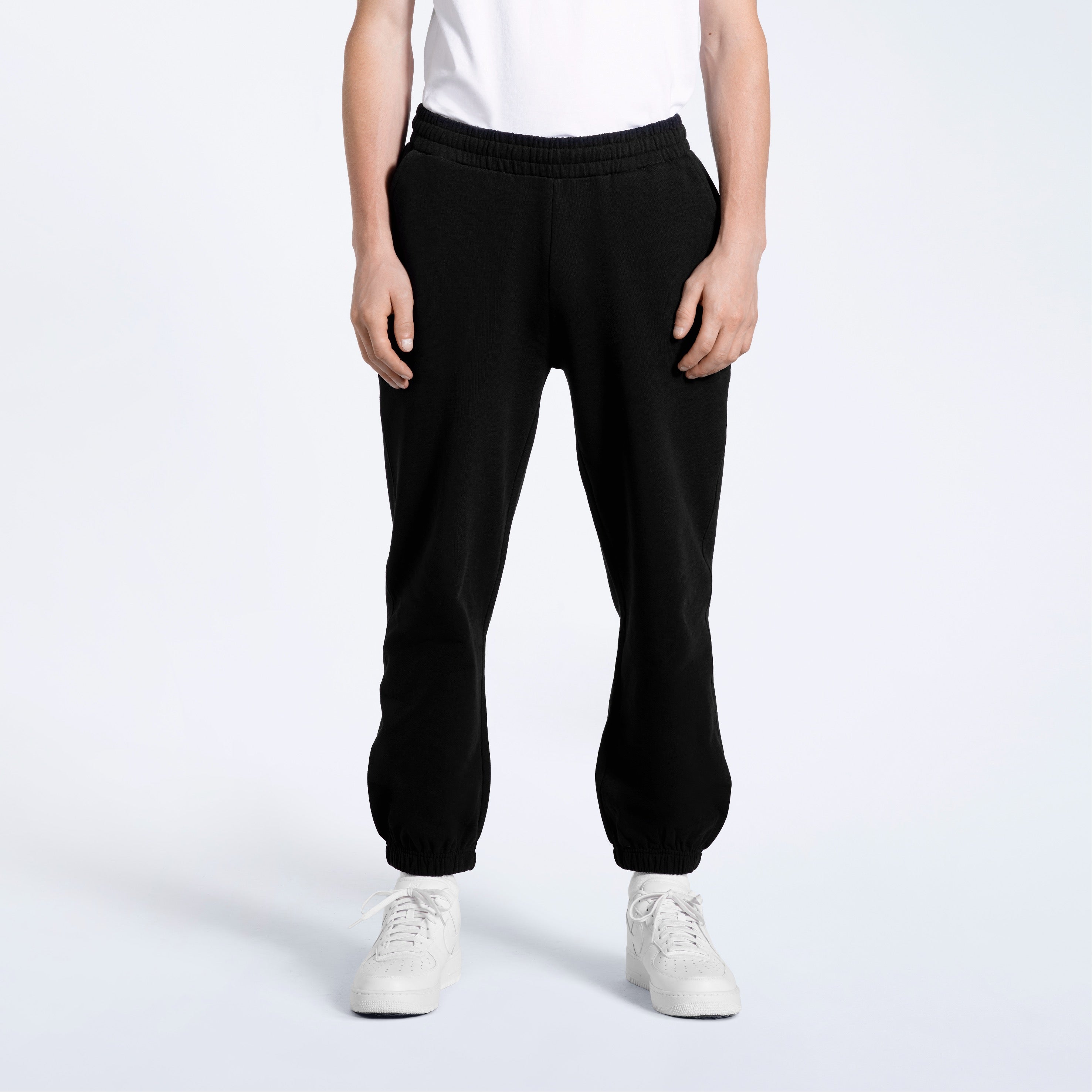A person with their arms by their sides, modelling a pair of men's black heavyweight organic cotton joggers.