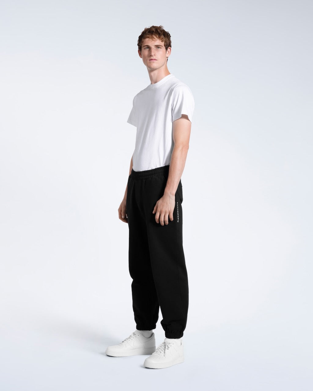 A man looking into the camera, modelling a pair of black heavyweight organic cotton joggers.